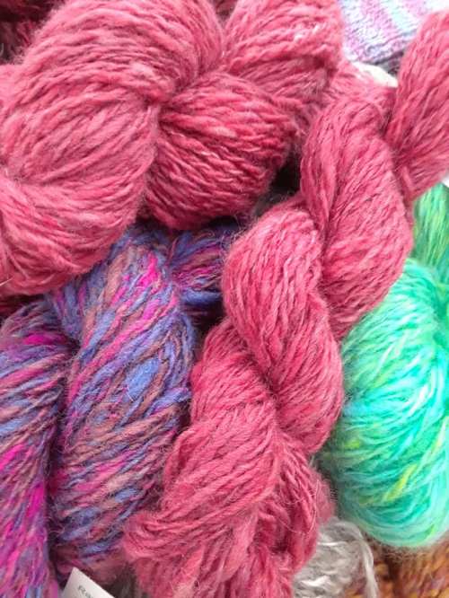 A close-up of various yarns in shades of pink, purple, and green, showcasing their textures and colors.