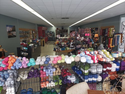 A colorful display of yarn in a craft store, with shelves and tables filled with various materials and supplies.