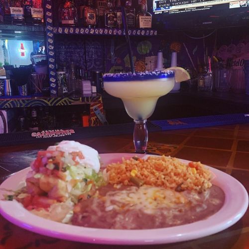 A plate of rice, beans, and salad next to a margarita in a vibrant bar setting.