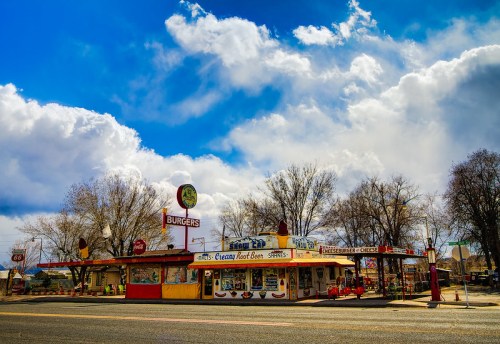 A colorful vintage burger diner with a retro sign, surrounded by trees and a dramatic sky.