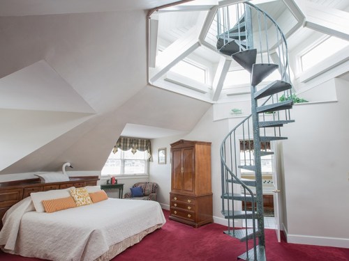 Cozy attic bedroom with a spiral staircase, skylights, and a wooden wardrobe, featuring a warm color palette.