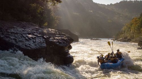 A group of people white-water rafting on a river, surrounded by rocky cliffs and lush greenery in the background.