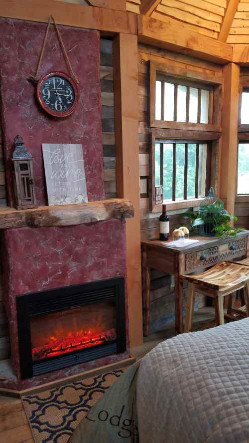 Cozy interior featuring a red fireplace, clock, wine decor, and wooden furniture with a plant and wine bottle.
