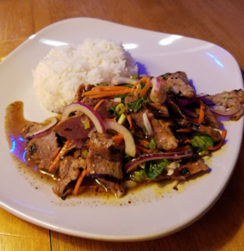 A plate of grilled meat with mixed vegetables and a side of white rice, drizzled with sauce.