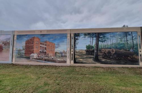 A mural featuring historical buildings and scenes of logging, set against a cloudy sky.