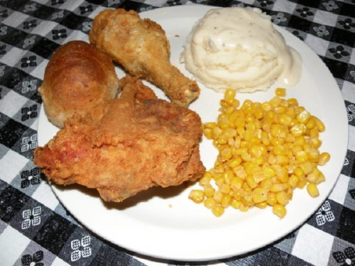 A plate of fried chicken, a biscuit, mashed potatoes with gravy, and corn on a checkered tablecloth.