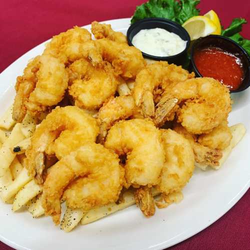 A plate of golden fried shrimp served with French fries, lemon, and two dipping sauces on the side.