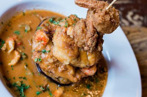 A plate of shrimp and grits topped with fried shrimp and garnished with parsley in a rich sauce.