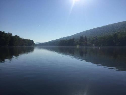 A serene lake reflecting a clear blue sky and surrounding green hills under bright sunlight.