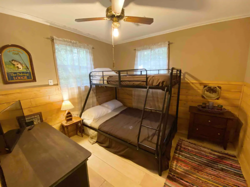 Cozy bedroom with a bunk bed, wooden walls, a ceiling fan, and natural light from two windows.
