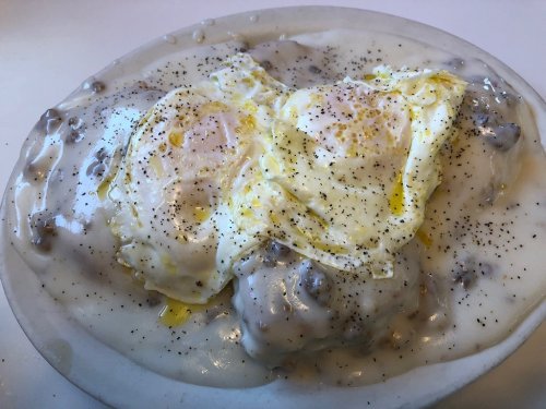 A plate of biscuits and gravy topped with two sunny-side-up eggs, sprinkled with black pepper.