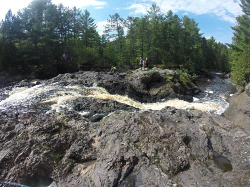 A rocky river with flowing water surrounded by lush green trees and people enjoying the natural scenery.