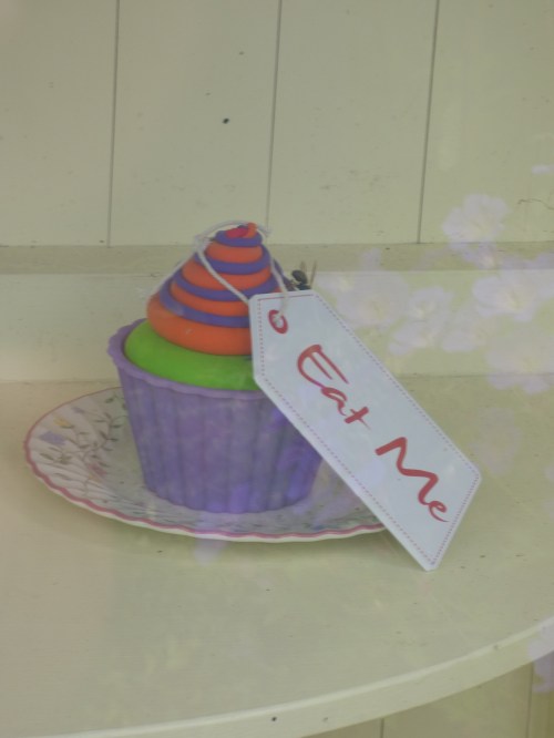 A colorful cupcake with a tag reading "Eat Me," displayed on a decorative plate.