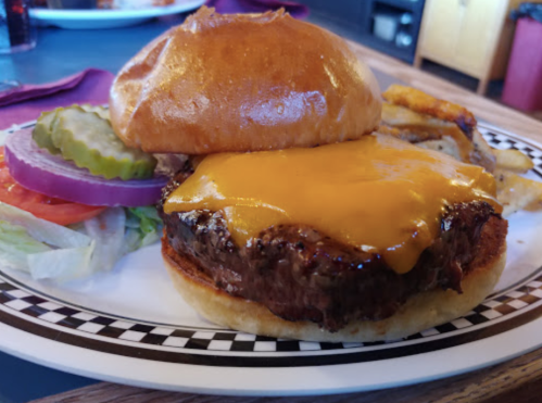 A juicy cheeseburger with melted cheddar on a toasted bun, served with pickles, tomato, and lettuce on the side.