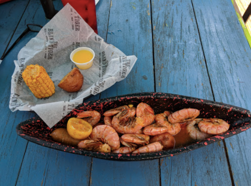 A seafood platter with shrimp, lemon, and a side of corn and a biscuit on a blue wooden table.