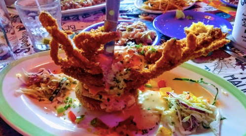 A plate featuring a large fried crab with a knife, surrounded by colorful sides and a vibrant table setting.