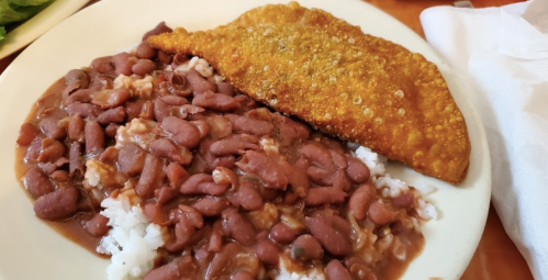 A plate of rice topped with red beans and a crispy fried fish fillet on the side.