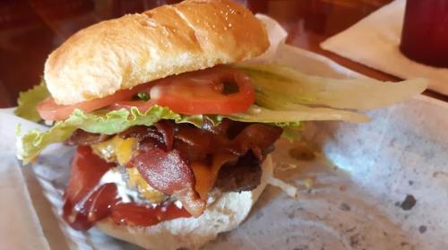 A close-up of a juicy burger with bacon, cheese, lettuce, and tomato on a sesame seed bun, served on a paper-lined plate.