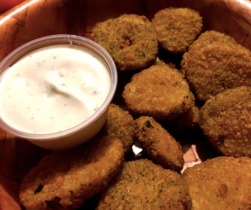 A wooden bowl filled with golden-brown fried food and a small cup of creamy dipping sauce.