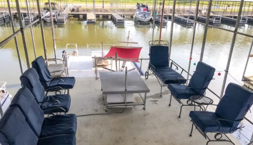 A covered dock area with several chairs and a table overlooking a calm waterway and boat slips.