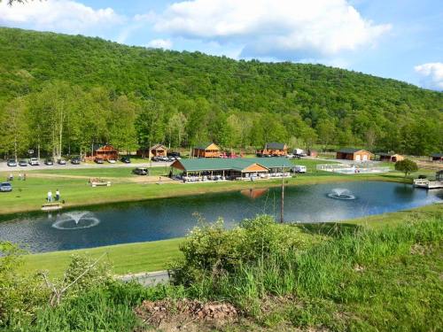 A scenic view of a green landscape with a pond, cabins, and people enjoying the outdoors under a blue sky.