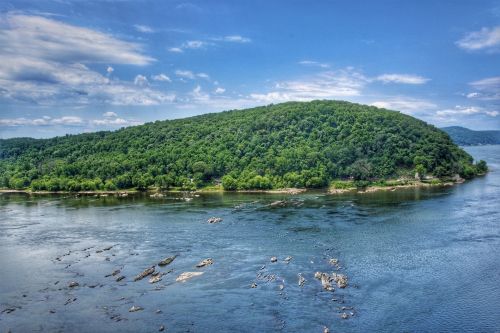 A lush green island surrounded by calm water under a blue sky with scattered clouds.