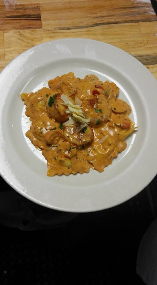 A plate of ravioli in a creamy tomato sauce, garnished with herbs and sliced almonds.