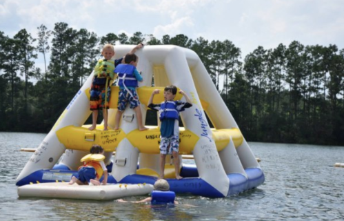 Children playing on an inflatable water structure in a lake, enjoying a sunny day.