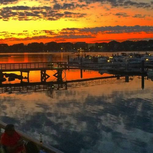 A vibrant sunset over a calm harbor, with boats and reflections in the water, creating a serene atmosphere.