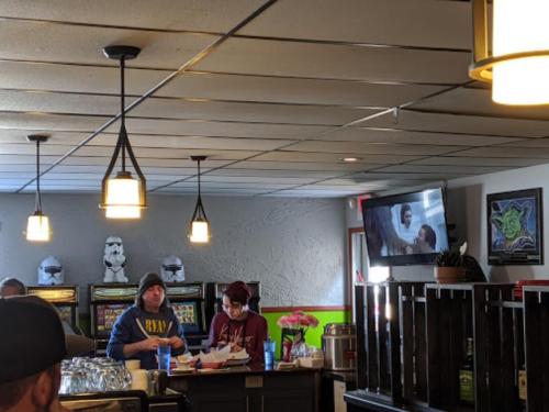 A cozy restaurant interior with two staff members at the counter, a TV showing a movie, and decorative lighting.