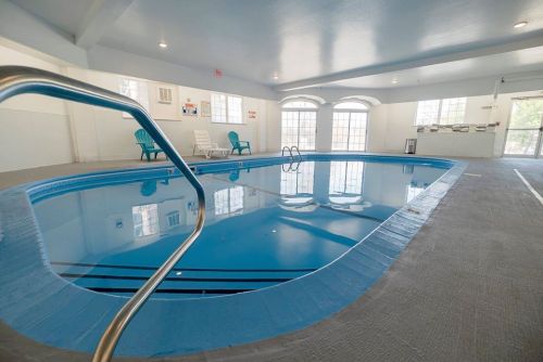 Indoor swimming pool with blue water, a ladder, and lounge chairs beside large windows.