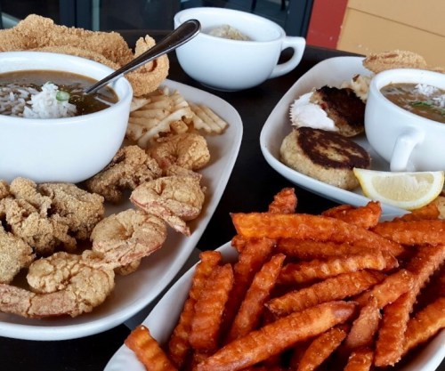 A spread of Southern dishes featuring shrimp, fried catfish, sweet potato fries, and bowls of gumbo with rice.