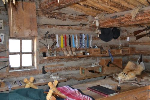 Interior of a rustic cabin with wooden walls, shelves displaying tools and artifacts, and a fur on the table.