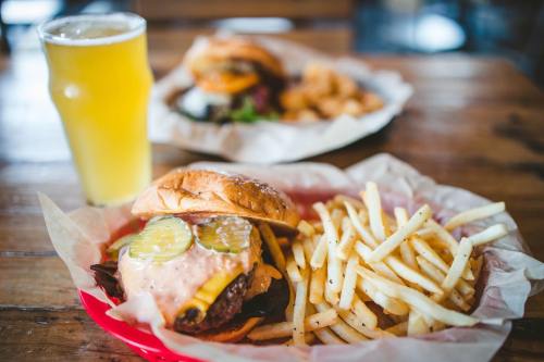A juicy burger with pickles and sauce, served with crispy fries and a glass of beer in a casual dining setting.