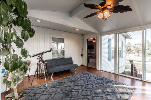 Bright sunroom with a telescope, a gray sofa, and large windows overlooking a garden.