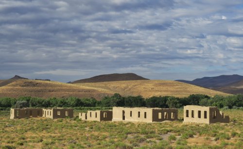 Ruins of a building in a grassy landscape, with rolling hills and a cloudy sky in the background.