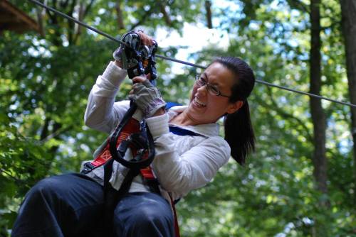 A person in a harness zip-lining through a forest, smiling with excitement as they grip the zip line.