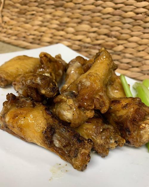 A plate of glazed chicken wings with a side of celery sticks, set against a woven background.