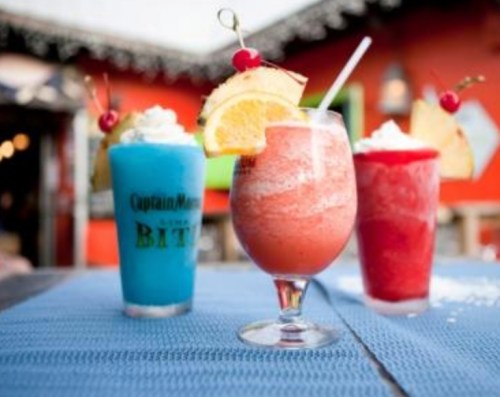 Three colorful cocktails on a table: a blue drink, a red slushy, and a pink frozen drink, garnished with fruit.