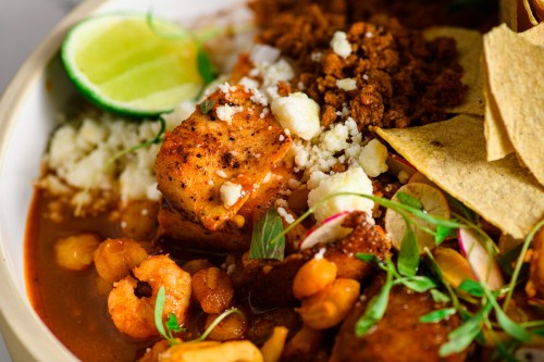 A close-up of a colorful dish featuring seasoned tofu, shrimp, beans, cheese, lime, and tortilla chips.