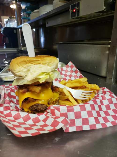 A large cheeseburger with bacon and lettuce, served with fries in a red and white checkered basket.