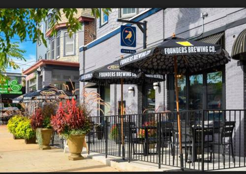 Outdoor seating area of a brewery with umbrellas, planters, and a vibrant street view.