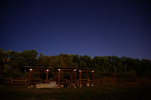 A wooden structure under a starry night sky, surrounded by trees and open land.