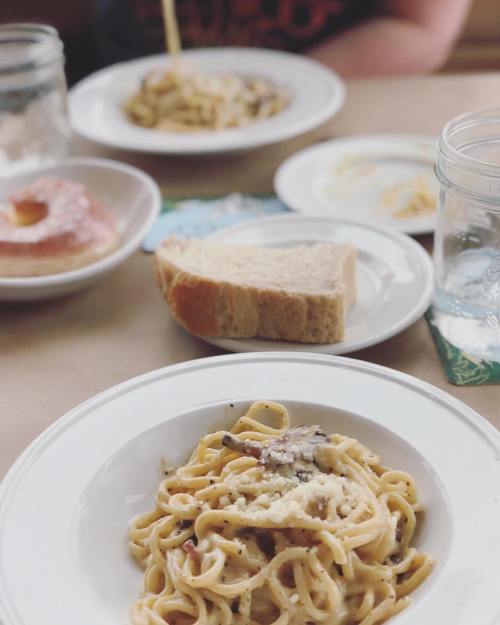 A table setting with plates of pasta, a slice of bread, a donut, and a glass of water.