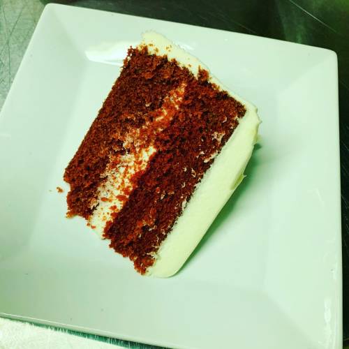 A slice of red velvet cake with cream cheese frosting on a white plate.