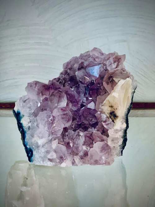 A cluster of purple amethyst crystals with a clear quartz section, resting on a light background.