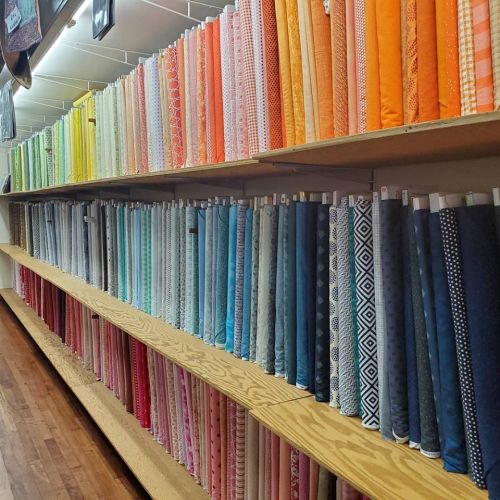 A colorful display of neatly arranged fabric rolls on wooden shelves in a craft store.