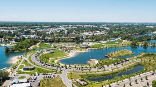 Aerial view of a park with winding paths, water features, and green spaces, surrounded by a cityscape.