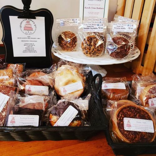 A display of assorted baked goods, including muffins and pastries, in clear packaging on a wooden table.