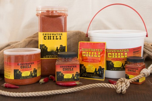 Various containers of Chugwater Chili seasoning, including jars, bags, and a bucket, displayed with red chili peppers.
